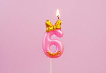 Burning pink birthday candle with golden bow and word happy on pink background, number 6.