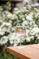 Refreshing Gin and Tonic with Juniper Berries and Mint in an Elegant Wine Glass - Summer Cocktail Served on a Wooden Table in a Garden Setting