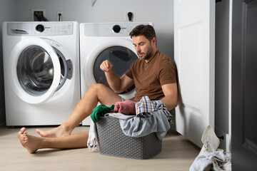 man sorting clothes near washing machine. man sits on the floor of a house near a washing machine with dirty clothes.man holding a dirty sock sitting by the washing machine, dirty shoes, dry cleaner.