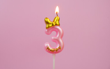 Burning pink birthday candle with golden bow and word happy on pink background, number 3.