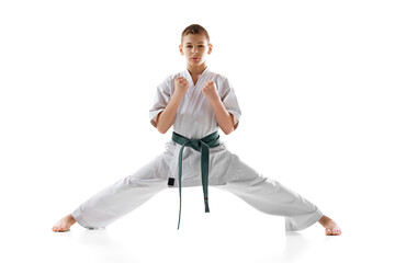 Teen boy, karate athlete posing in white kimono with green belt with focus and determination isolated on white studio background. Concept of sport, martial arts, combat sport, active lifestyle