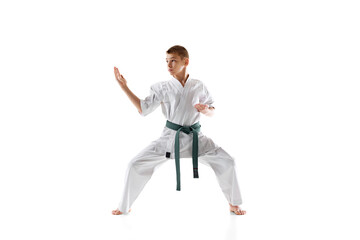 Teen boy in white karate and green belt demonstrating skills in stance, practicing isolated on...