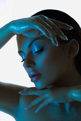 Beauty Woman posing with shimmering blue-tinted skin makeup, highlighted by cool studio light