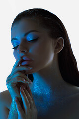 Woman beauty face is illuminated by a bright blue light, casting a striking contrast on her features