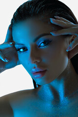 Beauty woman poses with glowing blue lights accentuating her eyes and complexion against a dark...