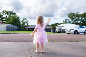 Happy little girl on driveway waving goodbye to neighbours cars