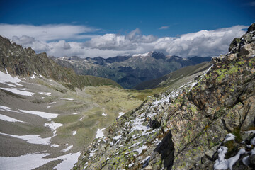 Panoramic vista of rocky mountains under a vast blue sky, patches of snow visible