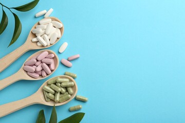 Different vitamin pills in spoons and green leaves on light blue background, flat lay. Space for...