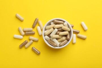 Different vitamin capsules on yellow background, flat lay