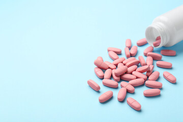 Vitamin pills and bottle on light blue background, closeup. Space for text