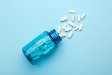 Vitamin pills and bottle on light blue background, top view