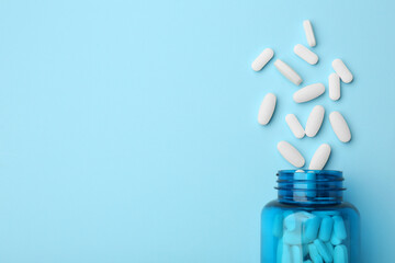 Vitamin pills and bottle on light blue background, top view. Space for text