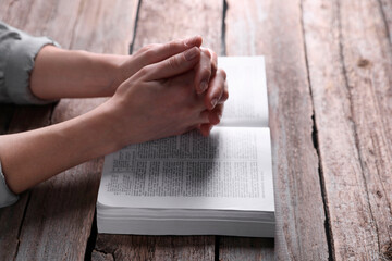 Religion. Christian woman praying over Bible at wooden table, closeup