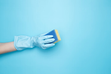 Womans hand in rubber glove holds yellow dishwashing sponge. House cleaning. Copy space