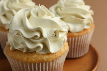 Tasty vanilla cupcakes with cream on dark beige background, closeup