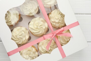 Tasty cupcakes with vanilla cream in box on white wooden table, top view