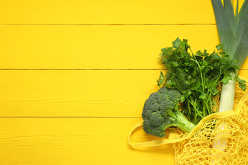 String bag with fresh vegetables and herbs on yellow wooden background, top view. Space for text