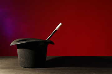 Magician's hat and wand on black wooden table against color background, space for text