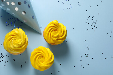 Delicious cupcakes with bright cream, party hat and confetti on light blue background, flat lay....