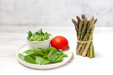 Bunch of fresh asparagus on wooden table, salad and tomato on a plate. Healthy food concept.  