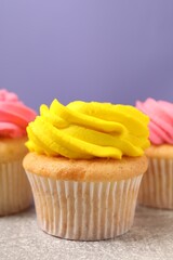 Delicious cupcakes with bright cream on gray table against violet background, space for text