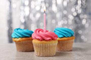 Delicious cupcakes with bright cream and burning candle on grey table, closeup
