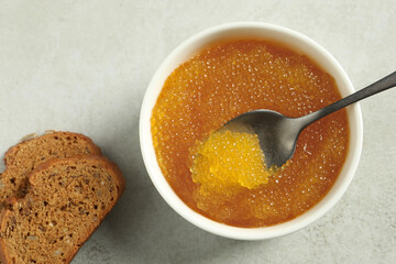 Fresh pike caviar in bowl, spoon and bread on light grey table, top view