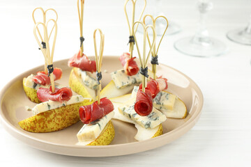 Tasty canapes with pears, blue cheese and prosciutto on white wooden table, closeup