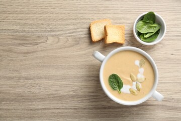 Healthy cream soup high in vegetable fats, bread and spinach on wooden table, flat lay. Space for text