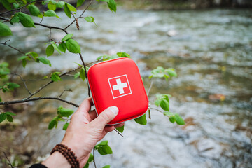 Person holding red first aid kit by river in natural landscape