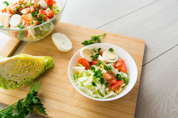 fresh vegetable salad, cabbage, tomatoes in a bowl on a wooden table