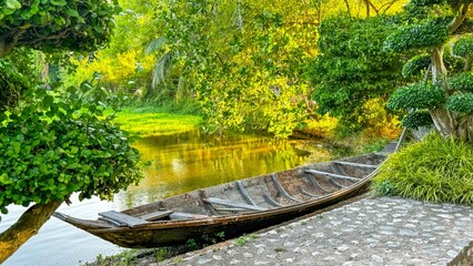 Weathered canoe lies beside vibrant pond in lush tropical garden, symbolizing eco-tourism and...