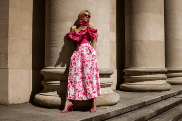 Elegant, stylish woman in pink floral dress and sexy high heels is sensually walking in the city on a sunny summer day. Outdoor shoot.