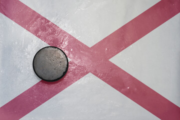 old hockey puck is on the ice with national flag of alabama state.