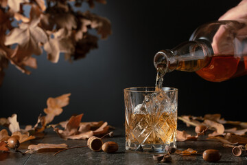 Whiskey with ice on a black table with dried-up oak leaves.