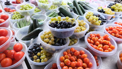 Plastic bowls of mixed fresh fruit and vegetables including grapes, tomatoes, and cucumbers at local greengrocer in Somerset, England UK
