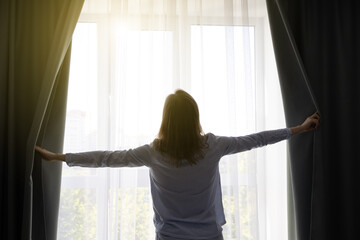 Woman is opening curtains near the window. Sunny day. Sunshine and warm at home.
