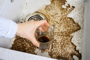 Woman is washing a dirty cup. Clogged drain water in wash basin sink. Dirty sink by coffee. Close...