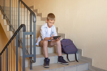 The boy is sitting on the stairs with a phone in his hands, playing games after school