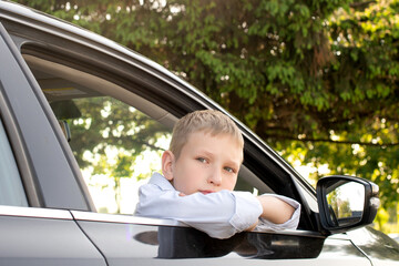 A cute boy looks out the car window and is sad. Open car window, long trip, family day