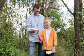 Dad showing paper plane to happy son outdoors, spending time together in nature