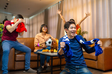 Group of Asian people friends sit on sofa watching and cheering football or soccer games...