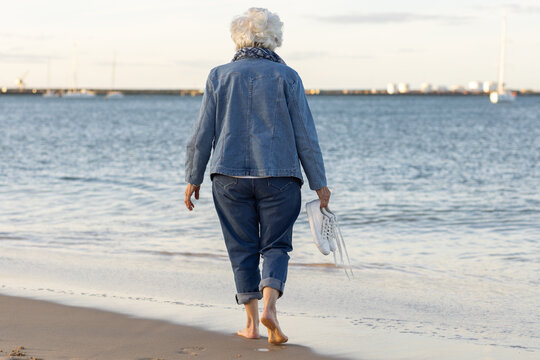 elderly woman wearing denim seen from behind walking on the beach