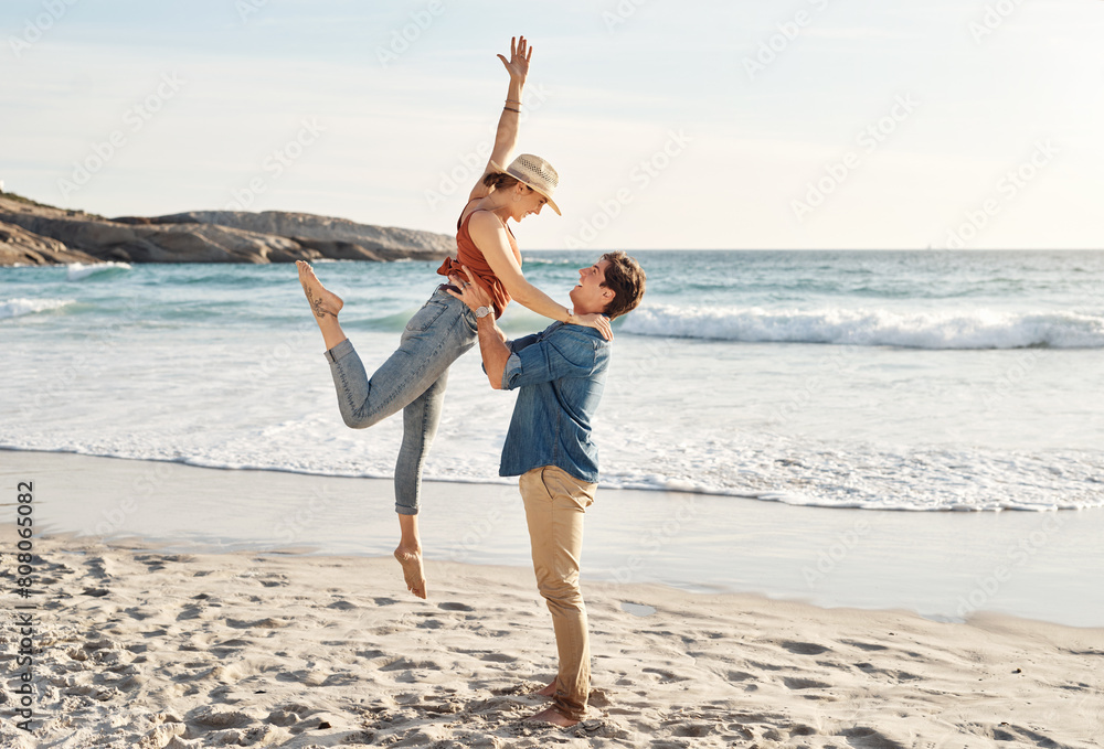 Canvas Prints Happy, lifting and couple at beach with love, summer and travel for vacation by ocean. Man, woman and hug at sea on sand with romance, smile and freedom or peace for holiday by water in Greece