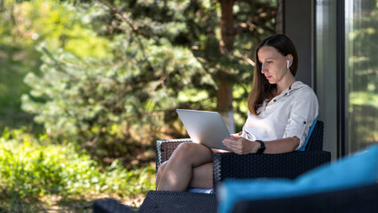 Young freelance woman using laptop sitting at the terrace in shade