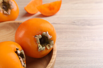 Delicious ripe persimmons on light wooden table, closeup. Space for text
