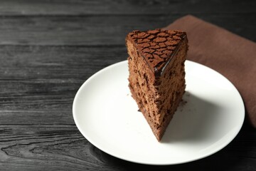 Piece of delicious chocolate truffle cake on black wooden table, closeup. Space for text