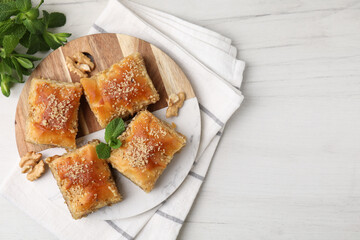Eastern sweets. Pieces of tasty baklava on white wooden table, top view. Space for text