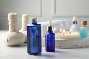 Spa composition. Bottles of cosmetic products, herbal bags, towel and burning candle on light table