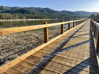 A serene mountain lake reflects azure skies, bordered by a wooden boardwalk with a walking bridge, embracing nature's tranquility.